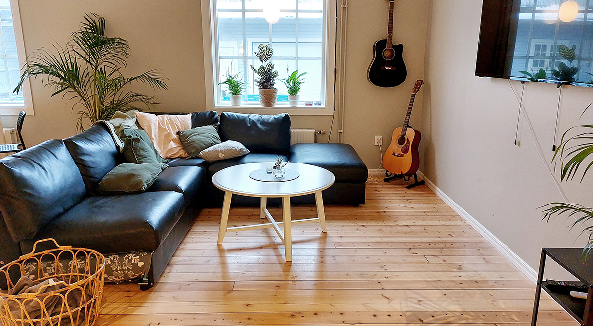 Vardagsrum med en bild på en svart skinnsoffa, två gitarrer, vitt soffbord och tv på väggen.